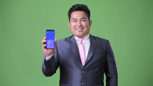 Young Handsome Overweight Asian Businessman Against Green Background