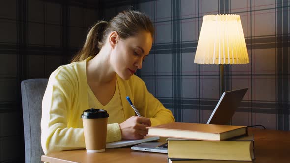 Business Woman in a Yellow Sweater is Pensively Writing Notes in Front of a Laptop