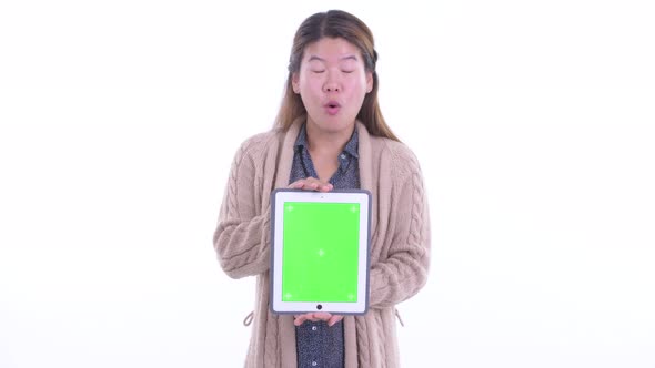 Happy Young Asian Woman Showing Digital Tablet and Looking Surprised Ready for Winter