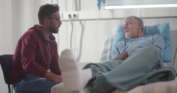 Adult Man Visiting Aged Father with Broken Leg in Hospital Ward