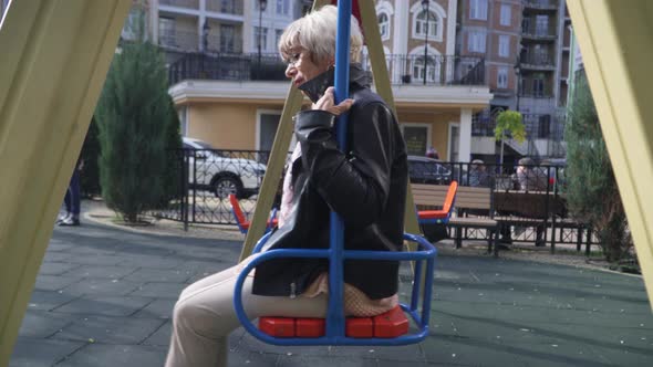 Side View Portrait Thoughtful Senior Beautiful Slim Woman Swinging on Swings on Playground