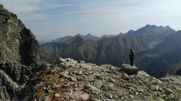 Drone Orbit Circle Around Hiker with Backpack Standing on Cliff