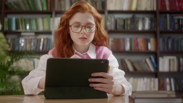 Attractive Student Woman with Red Hair Sketchig with Stylus on Digital Tablet Pc in Libraly