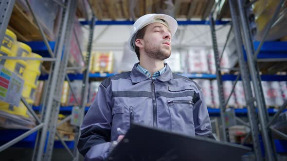 Concentrated Young Male Freight Agent Inspecting Warehouse Writing with Pen in Paperwork