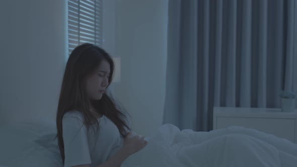 Asian beautiful girl in pajamas feel sick while sit on bed in bedroom.