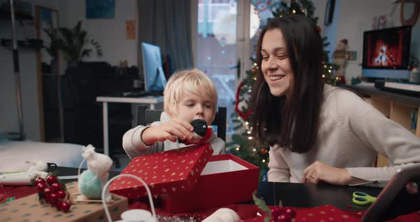 Playful Children Packing Handmade Christmas Gift with Mother in Living Room