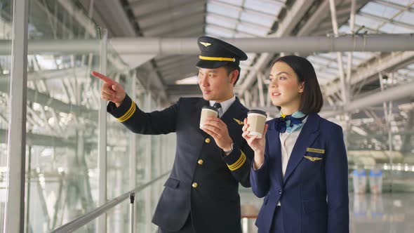 Asian airliner pilot and air hostess talking and drinking coffee together in airport terminal.