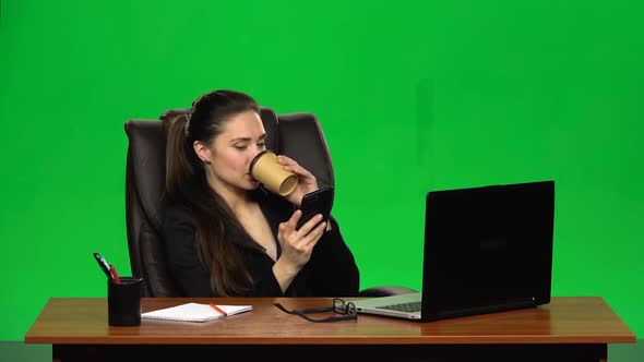 Business Woman Sitting at Desk in Leather Chair Writes Message on Cell Phone and Drink Coffee. Green