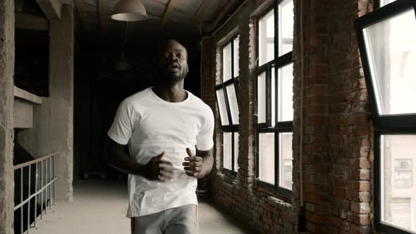 Fit black man in sport wear running near windows indoors