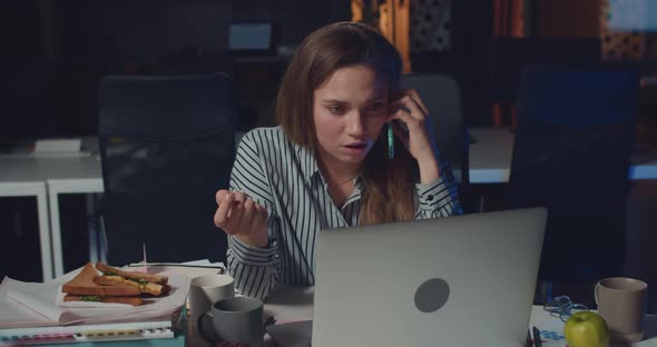 Woman Office Manager Working with Laptop and Talking on Smartphone with Sad Face. Young Woman
