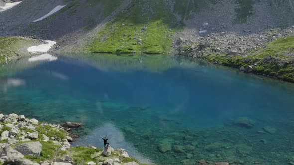 Aerial view of man traveler standing alone  hands up near emerald lake in mountains Arkhyz Russia