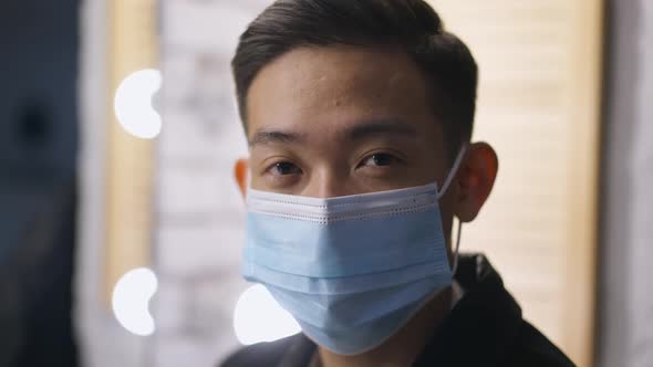 Headshot of Young Chinese Man in Covid Face Mask Looking at Camera with Serious Facial Expression