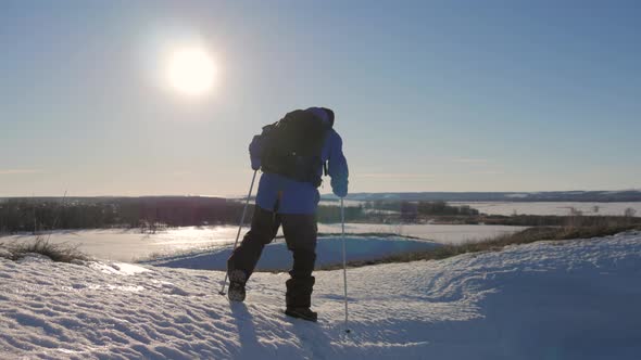 A Man with Backpack and Trekking Sticks Against the Backdrop of Winter Mountains