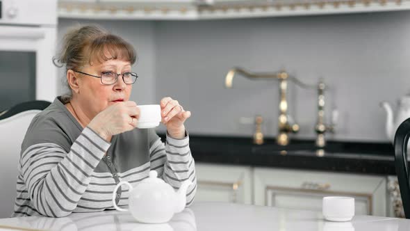 Pensive Middle Aging Confident Woman in Glasses Drinking Tea at White Cuisine Medium Shot