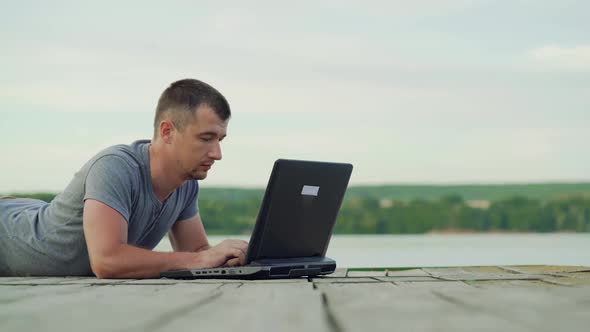 Man working on laptop outdoors. Wooden pier in the lake