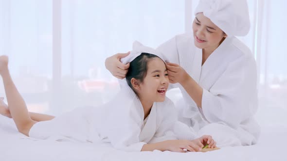 Mother with little daughter in bathrobes doing beauty treatment together at home.