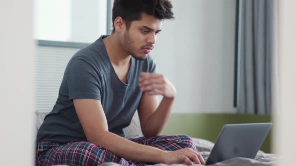 Confident Indian man wearing pajama typing by laptop