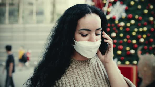 Young Beautiful Girl in in Warm Clothes Standing Near the Christmas Trees and Speaks By Phone on the