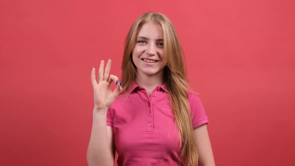 Happy Young Woman Showing Ok Sign with Fingers and Winking Isolated on a Red Background