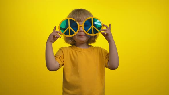 A Cute Little Girl is Taking Off the Funny Yellow Hippie Sunglasses