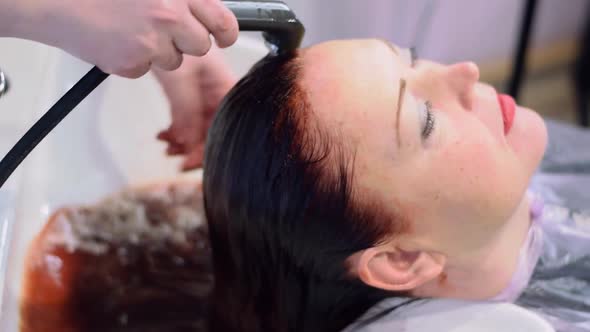 Hairdresser is washing the long red hair of the woman