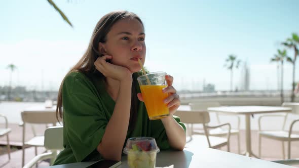 Handsome blonde woman wearing green t-shirt looking around and drinking orange juice