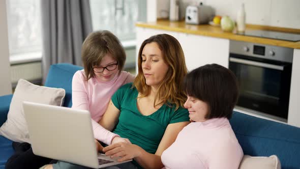 Happy Family with Two Daughters Down Syndrome Sitting on Sofa Have Fun Using Laptop