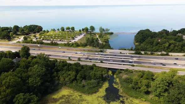 Aerial view of cars driving on a highway through a green park next to the Lake Ontario in Canada. Hi