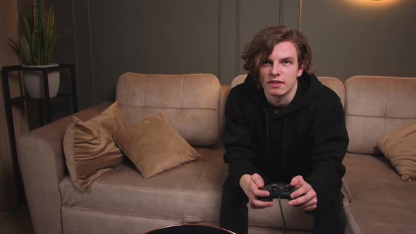 Excited Young Caucasian Man Gamer Holding Joystick Controller Playing Video Games Sitting on Sofa at