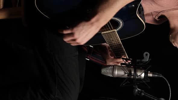 Vertical video. Young man plays an acoustic guitar on a black background
