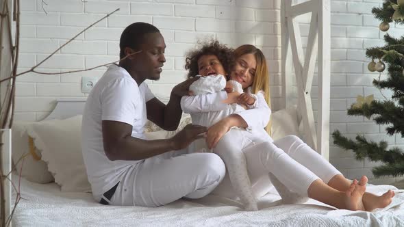 Young Happy Multi-ethnic Family of Mother, Father and Little Daughter Dressed in White at Background