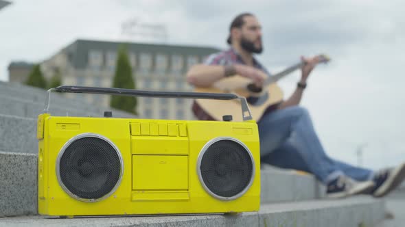 Vintage Yellow Tape Recorder Standing on Urban Stairs with Blurred Guitarist Playing at the