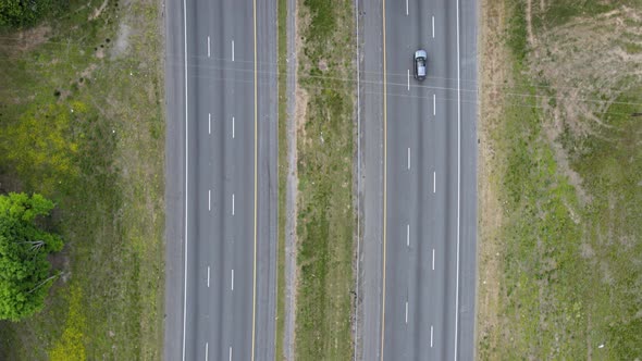 Cars driving under the overpass on a highway. The camera is pointed straight down flying over a busy