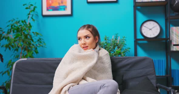 Caucasian American Woman Snuggling Into a Warm Blanket While Sitting on Her Sofa