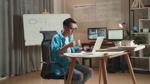 Asian Man Engineer Drinking Coffee While Using A Laptop To Work At The Office