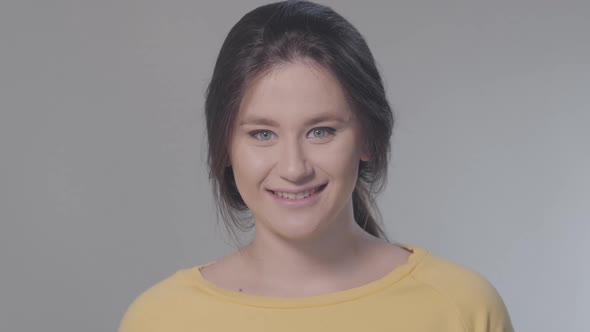 Close-up Portrait of Cheerful Young Caucasian Woman Grimacing at Camera on Grey Background