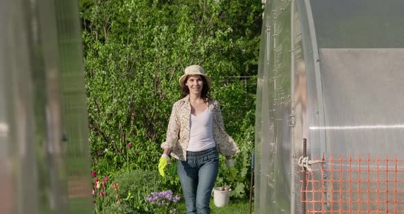 Beautiful Girl in Hat Works in Garden, Enters the Greenhouse. Young Woman Farmer Opens Door