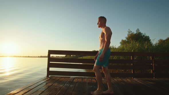 The Young Man is Walking to the Edge of the Pier and Raising His Hands