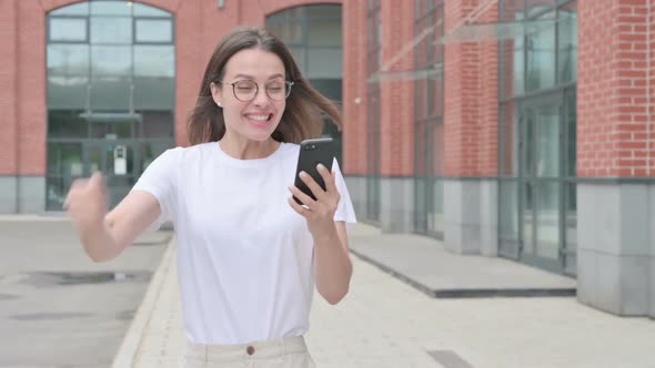 Young Woman Celebrating Success on Smartphone while Walking on Street