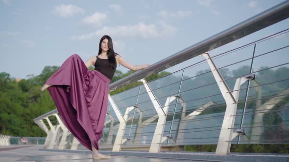 Wide Shot of Beautiful Ballerina Holding Bridge Handrail and Raising Leg Up. Portrait of Confident