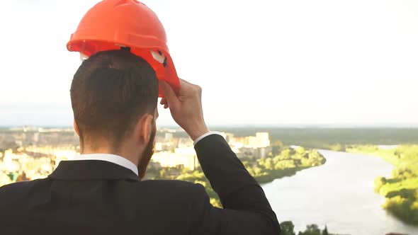 Young Engineer in the Yellow Helmet Looks at the Construction Site