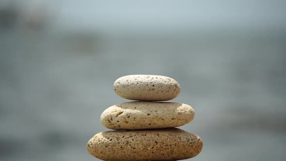 Woman Bilds Stones Pyramid on the Seashore on a Sunny Day on the Blue Sea Background