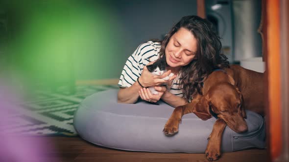 A Young Woman is Playing with a Kitten While Lying Next to a Big Dog