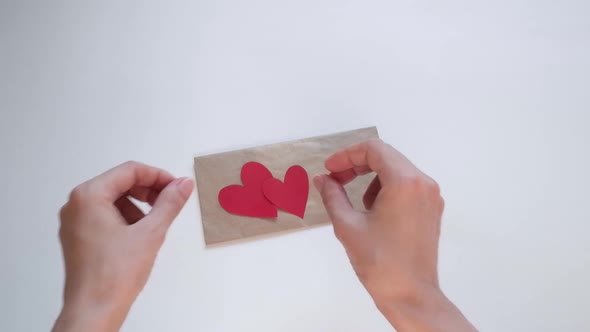 Hands Open an Envelope and Put a Red Heartshaped Valentine There for Valentine's Day