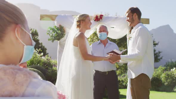 Caucasian bride groom and wedding officiant wearing face mask standing at outdoor altar