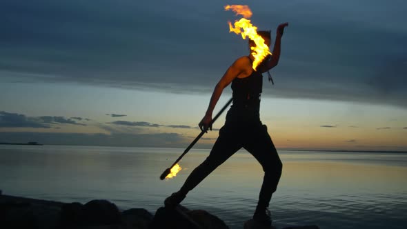 A Young Guy Puts on a Fire Show Against the Backdrop of a Sunset Sky and a River