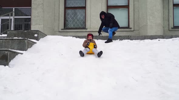 Father pushing kid on snow saucer riding down hill