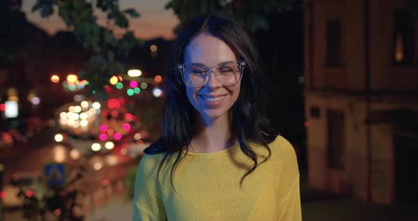 Woman in Glasses and Casual Clothes which Poses on Camera on Lights Night City background