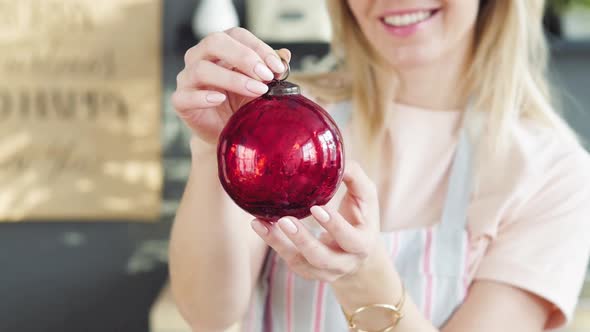 Blonde Holds Christmas Decoration and Smiles. close-up.Girl Shows a Product and Holds a Toy Ball