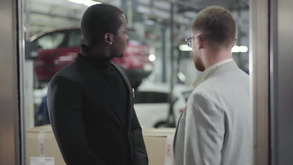 Portrait of Young Handsome African American Man Talking with Car Dealer in Showroom